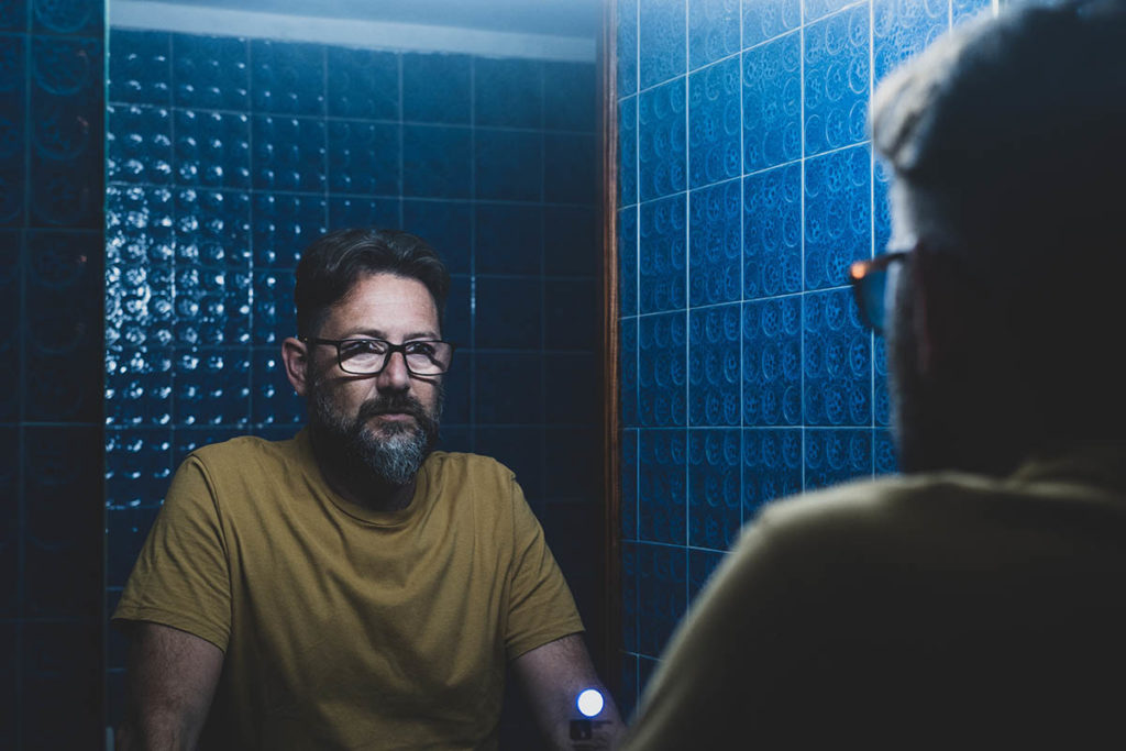 a man stares at his reflection in his bathroom mirror presumably after abusing common prescription drugs